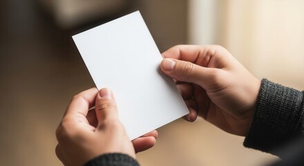 Obraz premium Close up of male hands holding empty white paper card mockup. Blank business card or postcard for design presentation. Person showing clear paper sheet with copy space for text.