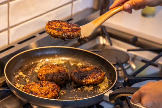 Home cook flipping seared burger patties in nonstick skillet on gas stove with wooden spatula