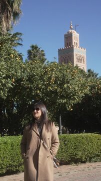 Young European tourist walking back through Lalla Hasna Park with Koutoubia Mosque minaret behind