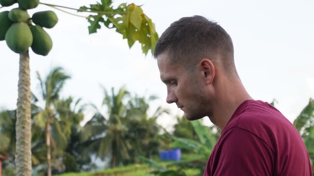 Man eating rambutan with papaya tree in the background