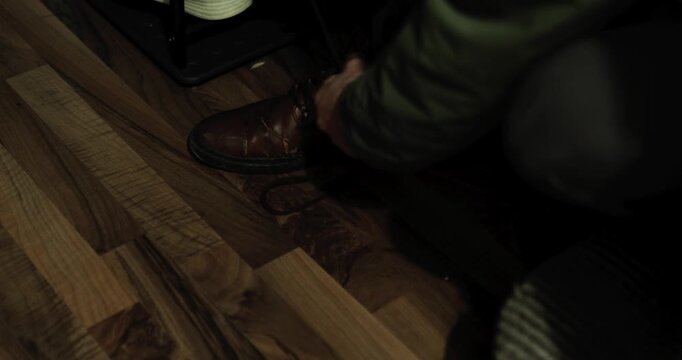 Close up capturing a tired blue collar worker unlacing his worn brown leather boots at the end of the day