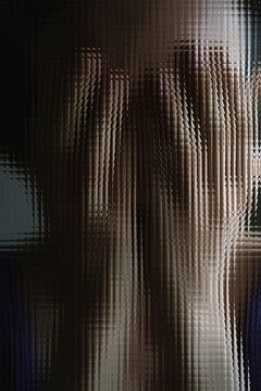 Hands on face behind fluted glass symbolizing anxiety and isolation