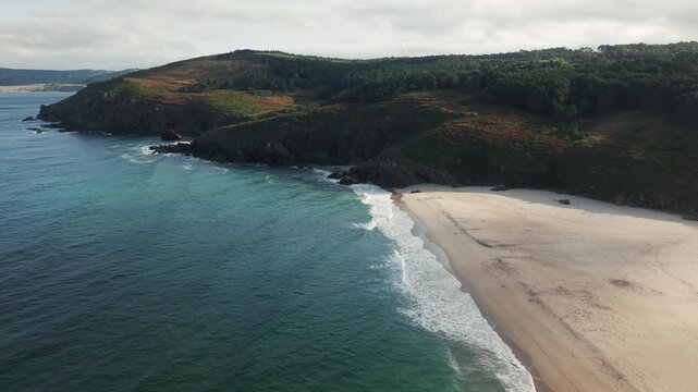 Drone pulling back and rising above Praia do Rostro beach in Galicia, Spain revealing Atlantic waves and rugged coastal landscape.