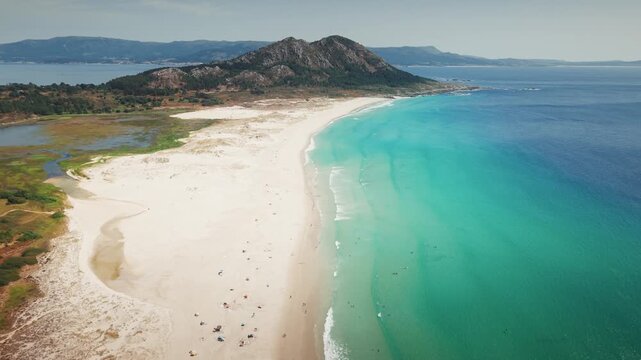 High drone shot flying forward above Praia de Louro revealing turquoise water, sandy beach and Monte Louro in Galicia, Spain.