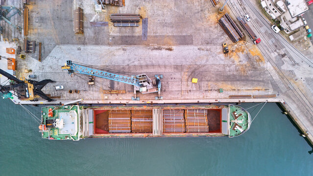 Pasai Donibane, Spain - 10 March 2026: Aerial view of a cargo ship berthed at the harbor, contrasting the ship's colorful hull with the weathered concrete and metal rebar cargo.