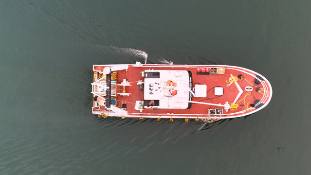 Pasai Donibane, Spain - 10 March 2026: Aerial view of a fishing boat with a red deck and white superstructure gliding through the dark, reflective waters of the harbor.
