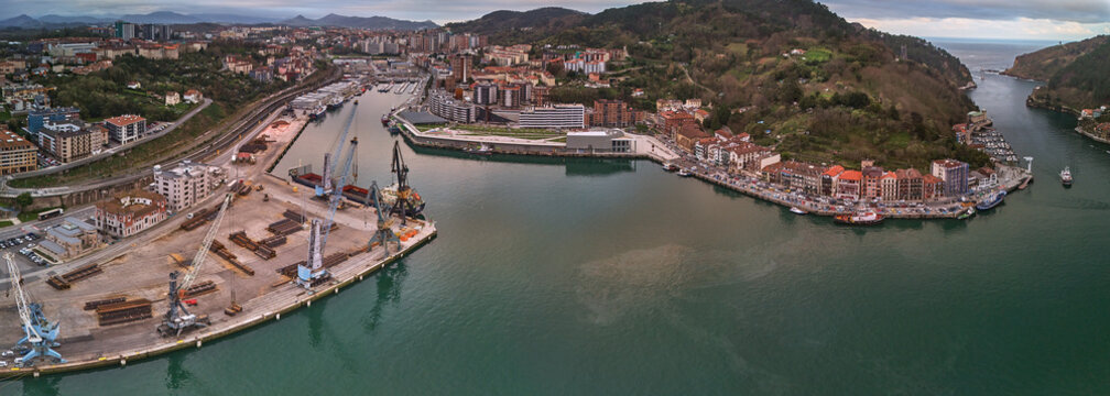 Pasai Donibane, Spain - 10 March 2026: Aerial view of the harbor where the dark water reflects the sky, contrasting with the colorful buildings and industrial cranes.