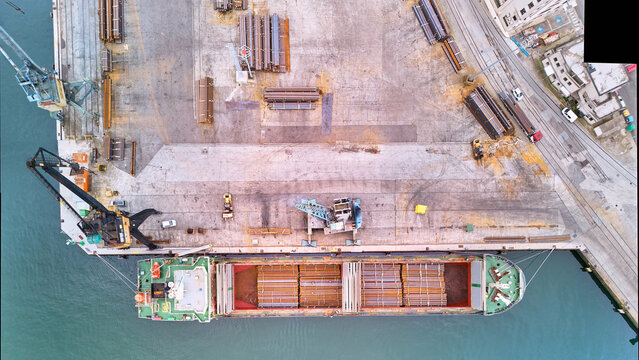 Pasai Donibane, Spain - 10 March 2026: Aerial view of a cargo ship docked at the harbor, contrasted against the weathered concrete and stacked metal rebar materials.