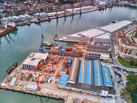 Pasai Donibane, Spain - 10 March 2026: Aerial view of the harbor with a shipyard, where the interplay of red brick structures and the gleaming silver roofs of warehouses meet the dark, still waters.