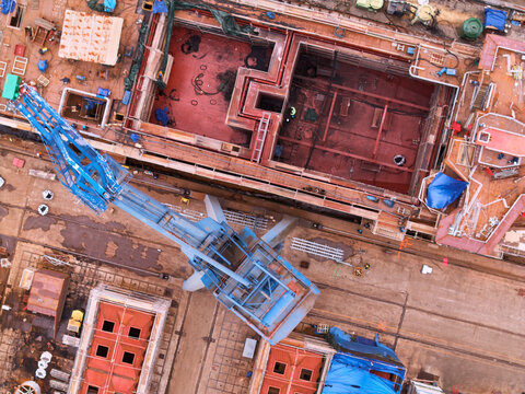Pasai Donibane, Spain - 10 March 2026: Aerial view of a large shipyard construction site with red flooring, surrounded by cranes and building materials, contrasts sharply with the blue machinery.