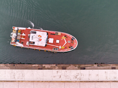 Pasai Donibane, Spain - 10 March 2026: Aerial view of a red and white fishing boat mooring, its hull cutting a path through the dark, rippled water near a concrete pier.