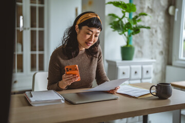 Woman managing finances at home office using smart phone