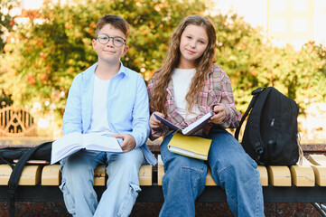 Schoolchildren sitting on bench studying outdoors © Serhii