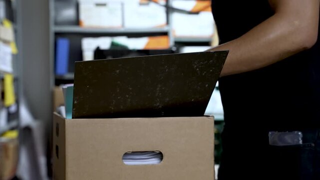 Person sifting through files in cardboard box, organizing documents in office storage