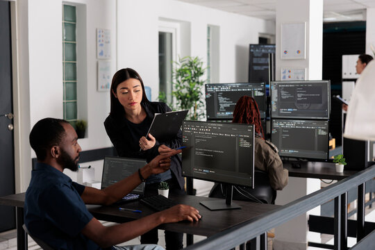 African american web developer using computer to write code and develop algorithm program in big data office room. System engineers working on user interface with html script and terminal window.