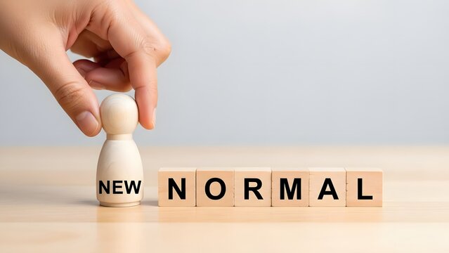 Hand is carefully placing a wooden human figure next to wooden blocks spelling "new normal", symbolizing adaptation to change.