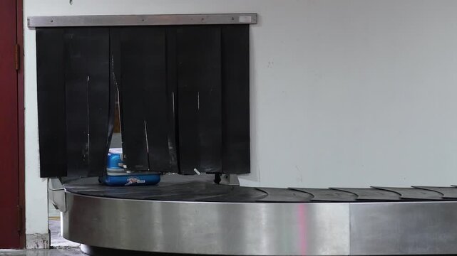 Baggage unloaded onto automatic conveyor belt and moves through gate on line from service area in airport after landing, luggage moving on carousel in arrival hall where tourists passengers pick up.