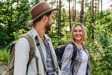 Fototapeta premium Young caucasian couple hiking together through forest trail smiling and enjoying nature
