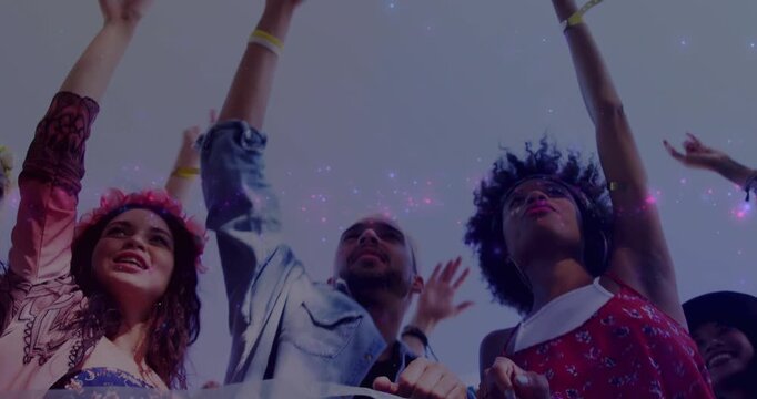 Three festival fans raising arms by barrier as pink-purple sparkles drifting past, sparking cheers
