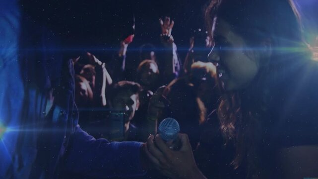 Left presenting mic toward right, right grabbing mic to sing, crowd reacting under blue lens flares