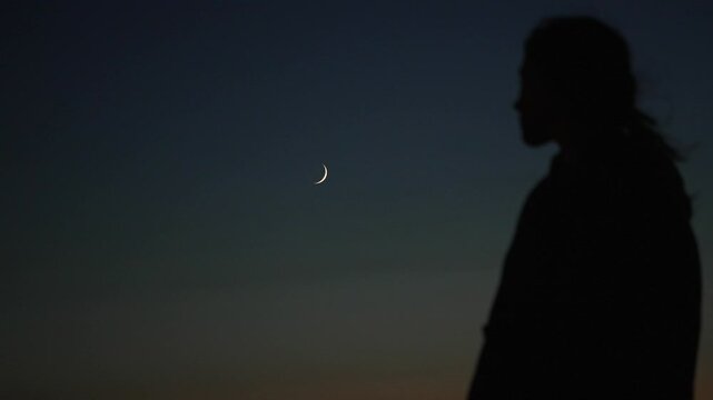 Woman silhouette stands under a crescent moon on Opal Coast, France.