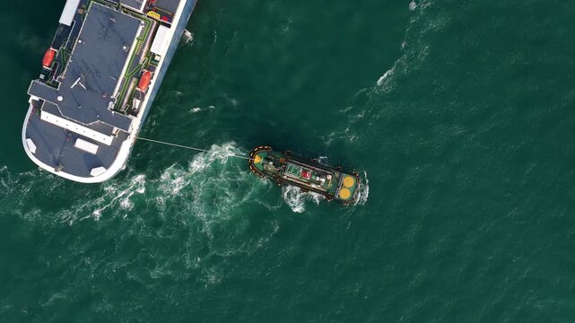Aerial view of tugboat towing large ship across green water