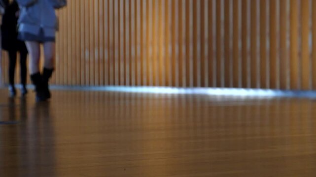 People walking in front of wooden vertical slats wall in slow motion, warm lighting and urban atmosphere. Suitable for lifestyle, business and cinematic background footage.