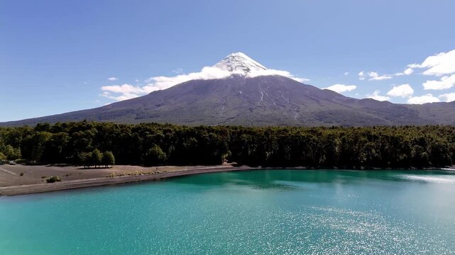 Begins over the emerald waters of Lake Todos los Santos, rising vertically and moving forward over the dense Valdivian forest canopy toward the snow-capped Osorno Volcano in Vicente P&eacute;rez Rosales Park