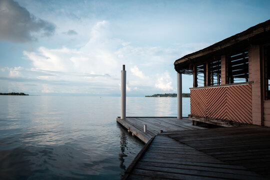 View of a wooden dock stretching into the calm, reflective waters towards distant islands beneath a cloudy sky, highlighting the stillness of the sea, Gizo, Gizo, Solomon Island.