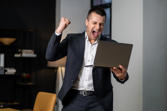 Male professional cheering and showing victory gesture after successful work moment indoors