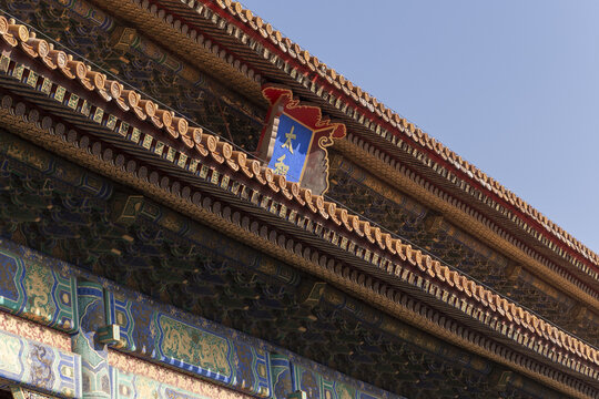 View of the ornate eaves with intricate carvings, painted details, and symbolic emblems against a clear sky, Beijing, Beijing, China.