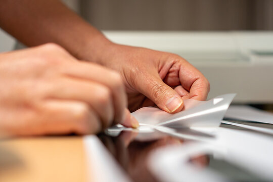 Production of car stickers from foil cut on a plotter. The worker holds a cover transfer foil in his hand and places it on a part of the stickers.