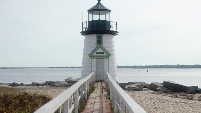 Smooth gimbal push-in toward Brant Point Lighthouse in Nantucket, Massachusetts, framed symmetrically along a wooden walkway with calm coastal waters and soft daylight.