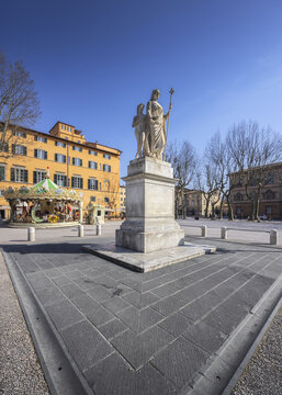 View of a white marble statue stands tall on a paved square, framed by the warm hues of surrounding buildings and the playful carousel, Lucca, Tuscany, Italy.