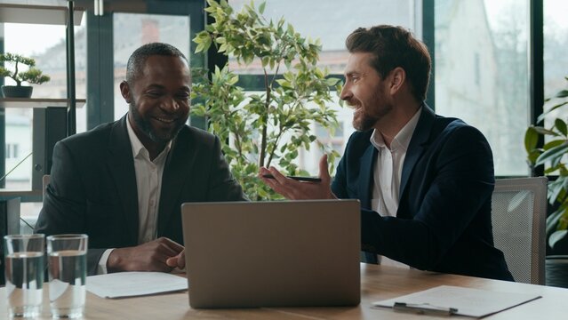 Diverse men colleagues business team sharing ideas laptop work discussing in office meeting smiling two multiracial businessmen excited happy emotional talking Caucasian man African American male