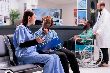 Asian female member of emergency hospital rapid response team filling out symptom form along with...