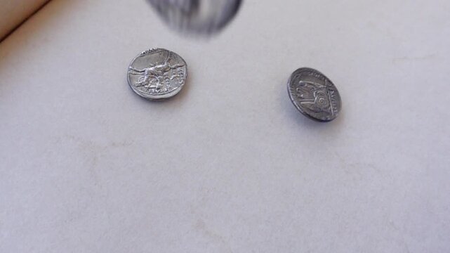 Ancient Roman silver coins falling on a neutral background.