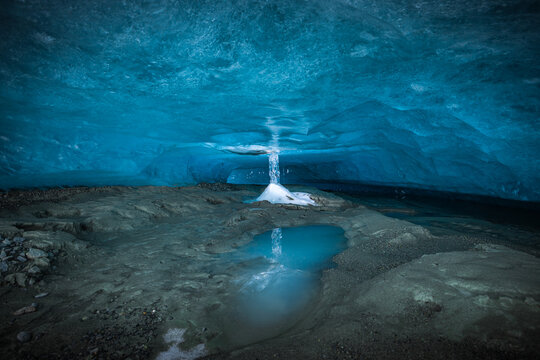 View of glacial meltwater cascading into a serene pool within an ice cave, creating a symphony of blues and grays, Lyngen, Troms, Norway.