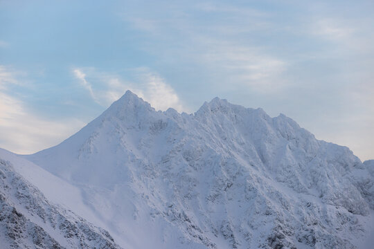 View of snow-clad peaks rise majestically against a pale sky, a wintry scene of stark beauty and peaceful solitude, Lyngen, Troms, Norway.