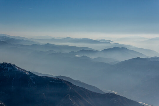 View of misty, blue-hued mountain ranges fading into the horizon under a clear sky, creating a serene and majestic landscape, Pir Chanasi, Azad Kashmir, Pakistan.