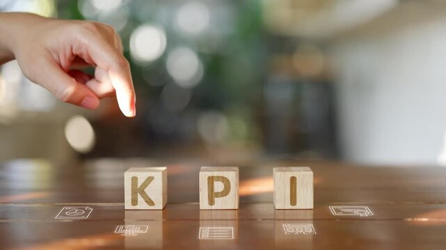 Hand of businessman pointing at KPI wooden blocks on table, concept of Key Performance Indicator, business growth, strategic planning, and performance measurement.