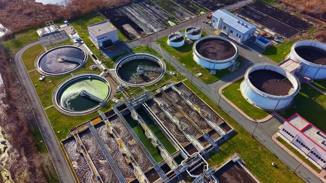 A wastewater treatment facility with several large circular and rectangular tanks for processing water. Equipment and buildings surround the tanks in a wide area.