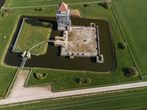 Aerial view of a medieval castle surrounded by a moat reflecting the sky, contrasting with the green fields, Sint Maarten, Noord-Holland, Netherlands.