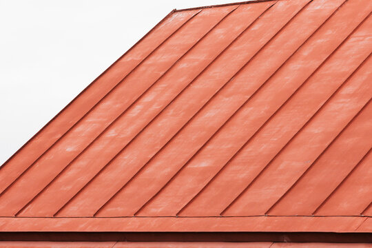 Close-up view of a red metal roof with diagonal panels and subtle weathered texture, creating a strong geometric pattern and minimalist architectural composition suitable for design and backgrounds