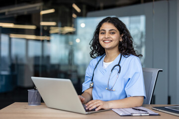 Female doctor working on laptop smiling at clinic