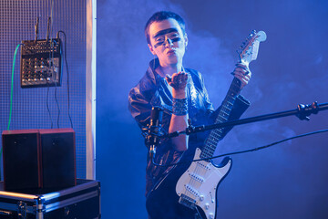 Obraz premium Cool artist blowing air kisses and acting flirty, playing guitar and having heavy metal style in studio. Sending kiss and being romantic or charming, singing alternative rock music with instrument.