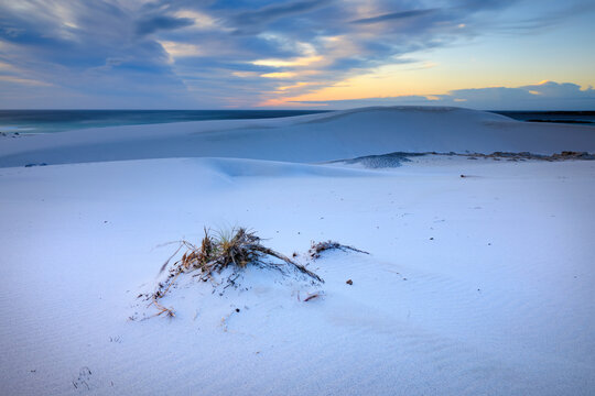 View of white sands meet the ocean under a sky painted with soft blues and golden hues at sunset, a serene coastal scene, Betty's Bay, Western Cape, South Africa.