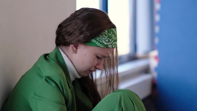 A girl with a bandana and long hair sits near a window, her face filled with stress and inner turmoil. The moment captures the mental strain of modern adolescence, where academic and social pressures