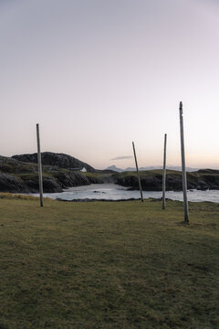 View of weathered wooden posts stand sentinel on a grassy headland overlooking the serene, rocky coastline at dusk, Clachtoll Beach, Sutherland, Scotland.