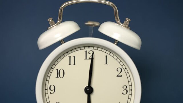 Classic white twin bell alarm clock vigorously ringing at six o'clock in the morning against a solid blue background, signifying the start of a new day or an important deadline